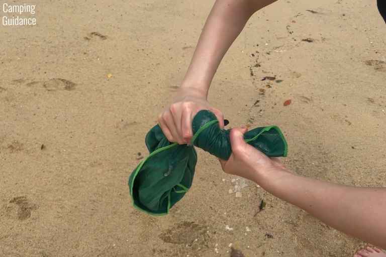 Wringing out excess seawater from the Wise Owl Towel after soaking it in seawater at a beach.