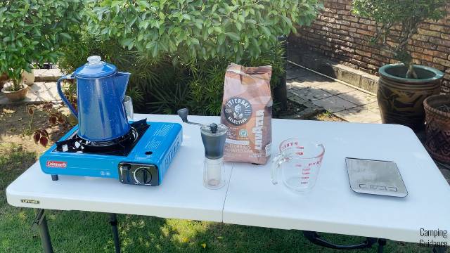 From left to right: I tested my 9 best camping percolators using a Coleman Portable Butane Stove, a Hario Mini Mill Hand Grinder, Lavazza medium-roast whole beans, a Pyrex measuring cup, and an Etekcity Digital Kitchen Scale.