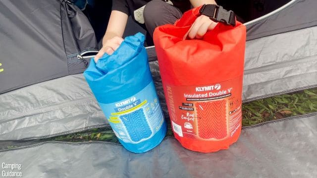 This is a picture of me holding the Blue packed up Klymit Uninsulated Double V (left) beside the Red packed up Klymit Insulated Double V (right).