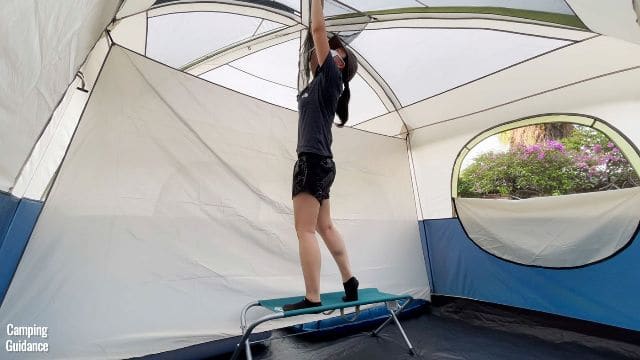 This is a picture of me standing on a Coleman bench to put up the gear loft, of the Ozark Trail 10-Person Cabin Tent, because I’m not tall enough.