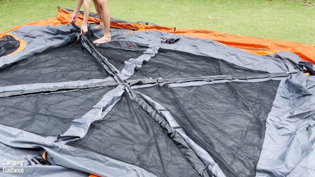 This is a picture of me inserting the fiberglass roof poles through the black and gray roof pole sleeves of the Core 10-Person Straight Wall Cabin Tent.