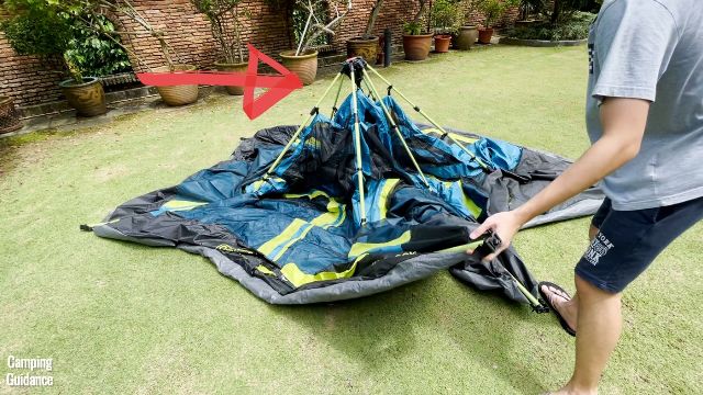 This is a picture of my brother unfolding the Coleman 10-Person Instant Tent, with the central hub still upright (red arrow pointing to the central hub).