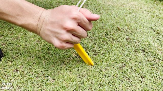 This is a picture of me using the provided yellow plastic stakes to stake out one of the guylines of the Coleman WeatherMaster 10-Person Tent.