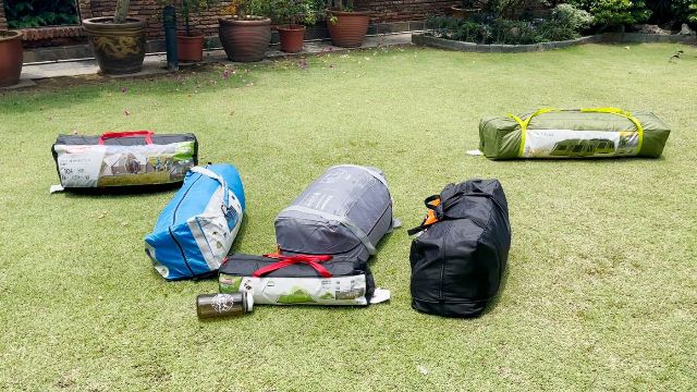 This is a picture of some of my best 10-person tents (packed up) in my yard. From left to right: Coleman WeatherMaster 10-Person Tent (black with red straps), Columbia Mammoth Creek 10-Person Tent (blue), Core 10-Person Straight Wall Cabin Tent (gray), Ozark Trail 10-Person Cabin Tent (black), Outdoor Products 10-Person Instant Tent (green). The smaller tent in front is a Coleman 2-Person Sundome Tent.