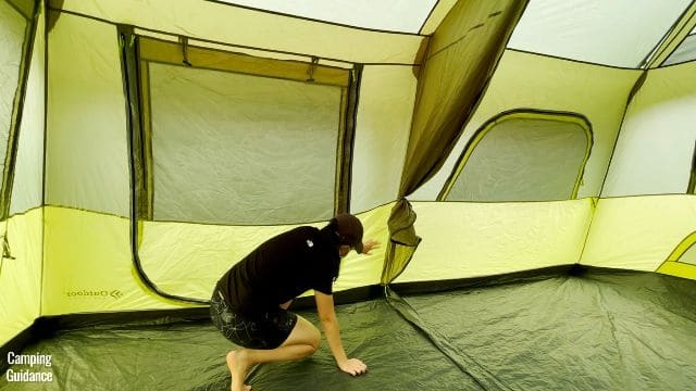 This is a picture of me touching the light green fabric at the bottom half of the Outdoor Products 10-Person Instant Cabin Tent.