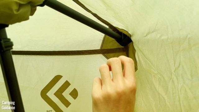 This is a picture of me securing the Velcro attachment of the rainfly of the Outdoor Products 10-Person Instant Cabin Tent to the tip of each extended eave.