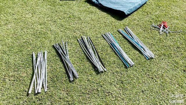 The 5 aluminum poles of the REI Base Camp 6 (1 is white, 2 are black, and 2 are blue). The 12 stakes and 4 guylines are to the extreme right.