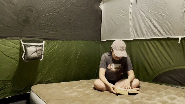 The author reading a book in a tent lighted by the BioLite AlpenGlow 500.